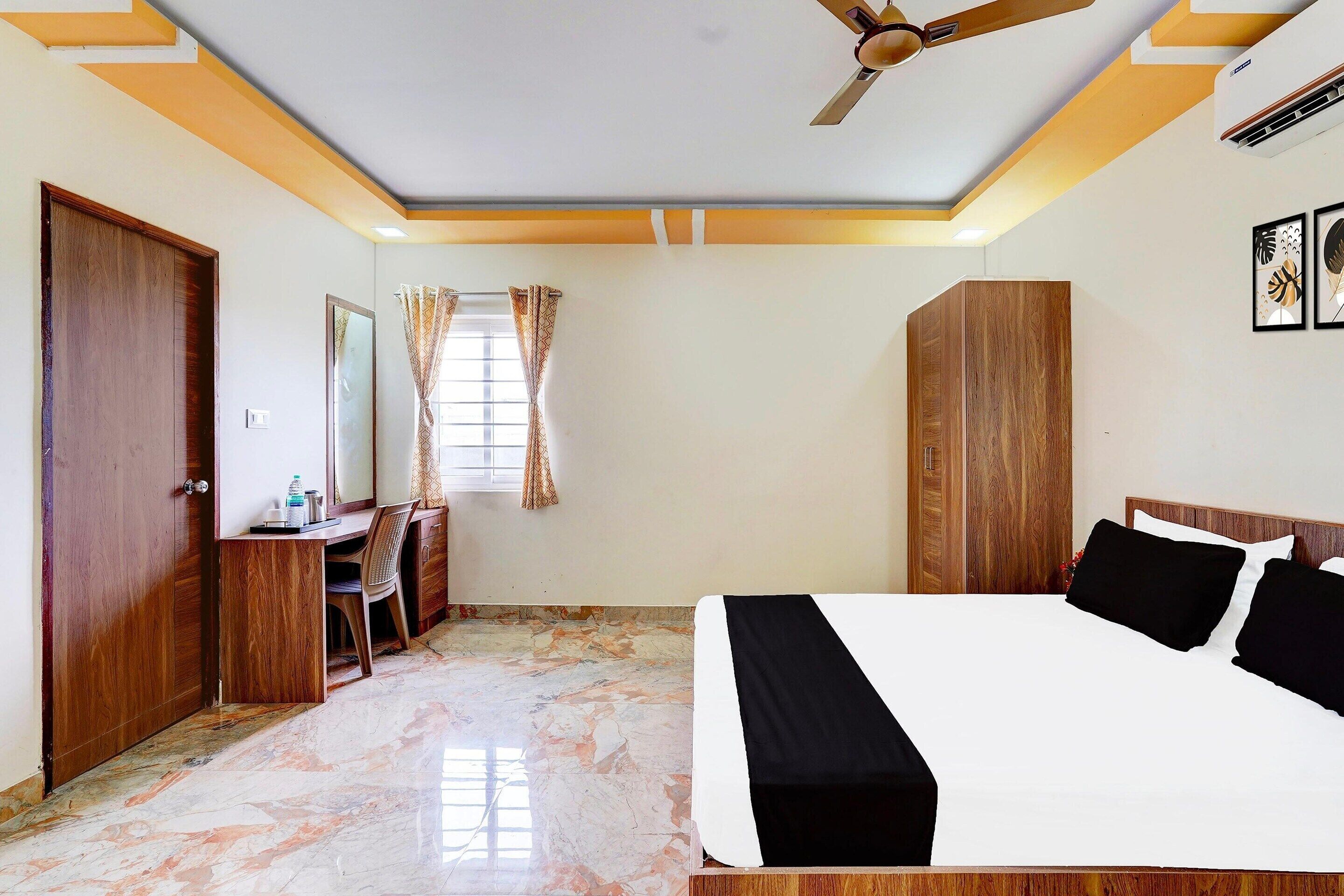 Habitación de hotel con cama, escritorio, silla, armario y ventilador de techo.