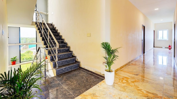 Un pasillo amplio con piso de mármol, una escalera con barandillas de metal y plantas en macetas.