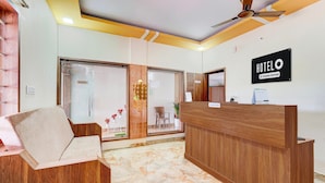 Zona de recepción de un hotel con un mostrador de madera, un cartel de recepción y un área de estar con una silla acolchada.