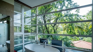 Un baño moderno con una bañera independiente, ventanas amplias y vistas a exuberante vegetación.