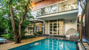 Una casa moderna de dos pisos con piscina, ventanas amplias y un balcón.