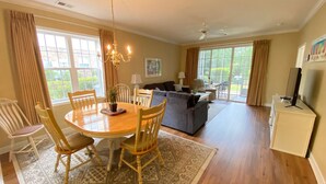 A spacious living room with a dining area, large windows, and a ceiling fan. - Havens 1311 Beautiful Condo! (North Myrtle Beach)