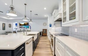 A modern kitchen with white cabinetry, a central island, pendant lighting, and a view into the dining area.