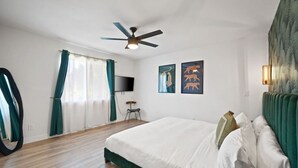 Una habitación de hotel con una cama, un ventilador de techo, un televisor y obras de arte en la pared.
