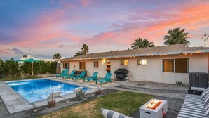 Un patio trasero con piscina, mobiliario exterior y zona de barbacoa.