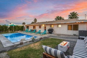 Un patio trasero con piscina, mobiliario exterior y zona de barbacoa.