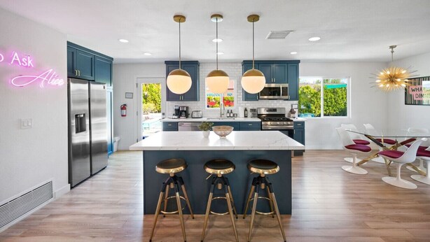 Cocina moderna con una isla central, taburetes de bar e iluminación colgante.