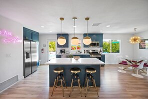 A modern kitchen with a central island, bar stools, and pendant lighting. - Retro Vibe Stay | Pool, Game Room, Sauna! Sleeps 8 (Palm Springs)