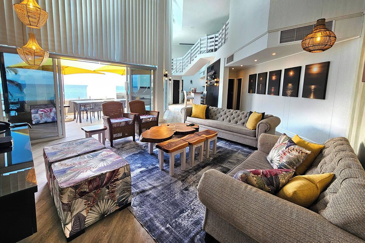 A spacious living area with a sofa, chairs, and a coffee table. There is a balcony with a view of the ocean.