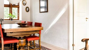 Een eetruimte met een houten tafel, rode bekleden stoelen, een hangende lamp en een raam met uitzicht op groen.