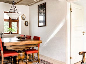 A dining area with a wooden table, red upholstered chairs, a hanging light fixture, and a window with a view of greenery.
