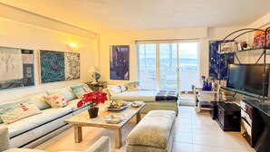 Un salon moderne avec un canapé, une table basse et un téléviseur. Il y a un balcon avec vue sur la ville.