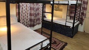 Une chambre de dortoir avec des lits superposés, des rideaux à motifs et un plancher en bois.