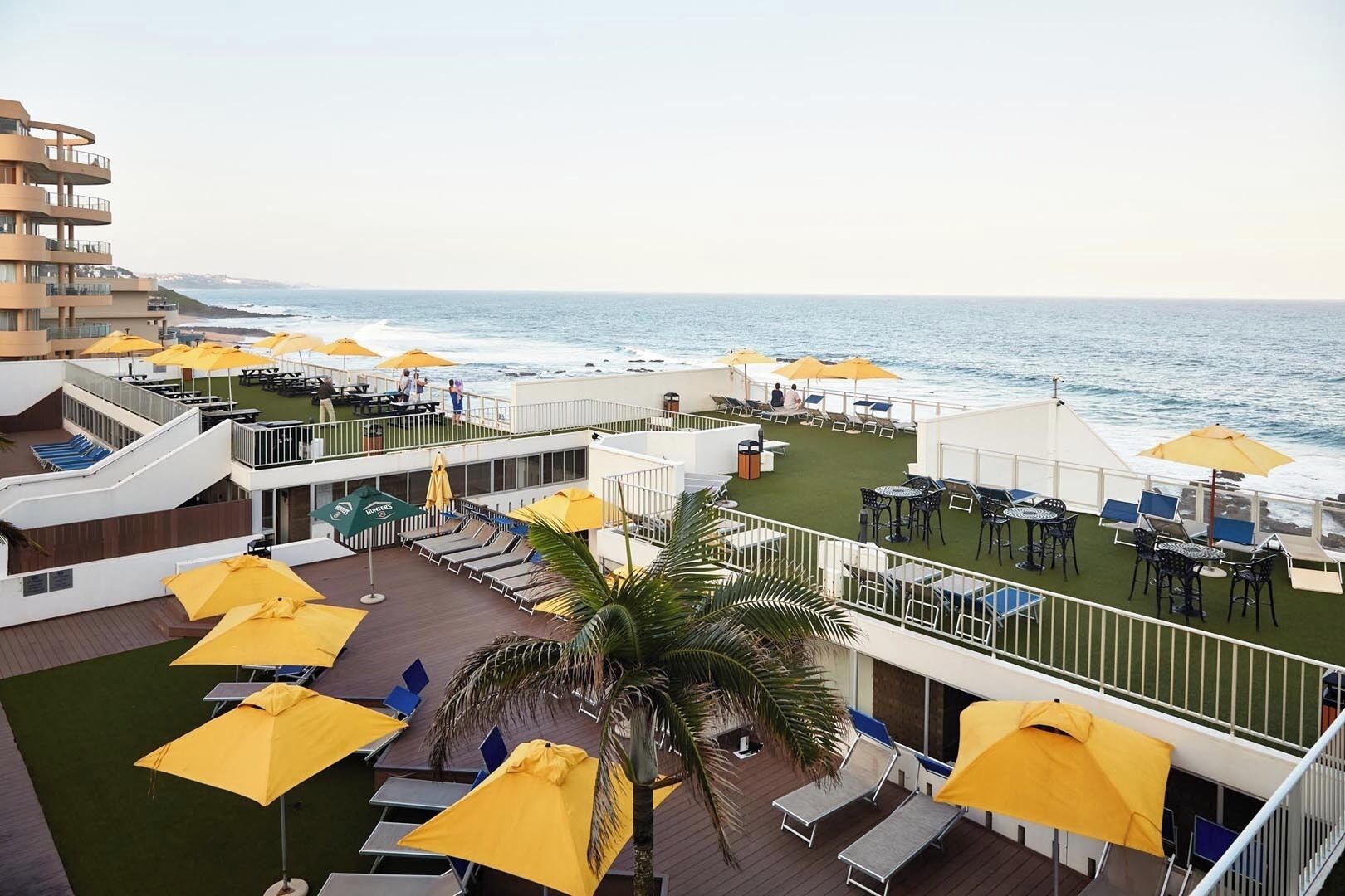 A multi-level outdoor deck with yellow umbrellas, lounge chairs, and tables overlooking the ocean.