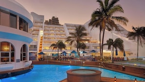 A resort pool area with a large pool, palm trees, and a modern building with multiple balconies. - Penthouse 712 at La Montagne by First Private Stays (Ballito)