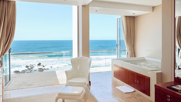 A modern bathroom with a bathtub, a chair, and a view of the ocean. - Penthouse 712 at La Montagne by First Private Stays (Ballito)
