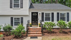 A two-story house with a front porch, a black door, and a brick staircase leading to the entrance.