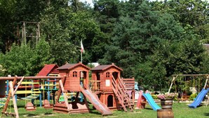 A playground with wooden play structures, including slides and climbing areas, surrounded by trees. - Single-storey Homes by the Lake, Jelen (Borne Sulinowo)