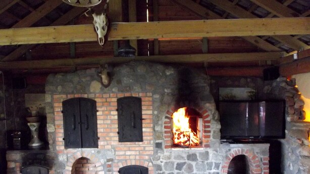 A rustic interior with a stone fireplace, wooden beams, and a television mounted on the wall. - Single-storey Homes by the Lake, Jelen (Borne Sulinowo)