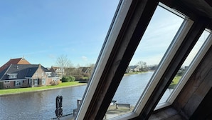 Une vue à travers une fenêtre donnant sur un canal, avec des maisons et un banc.
