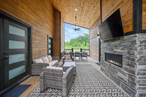 A covered outdoor seating area with wicker furniture, a stone fireplace, and a view of the outdoors.