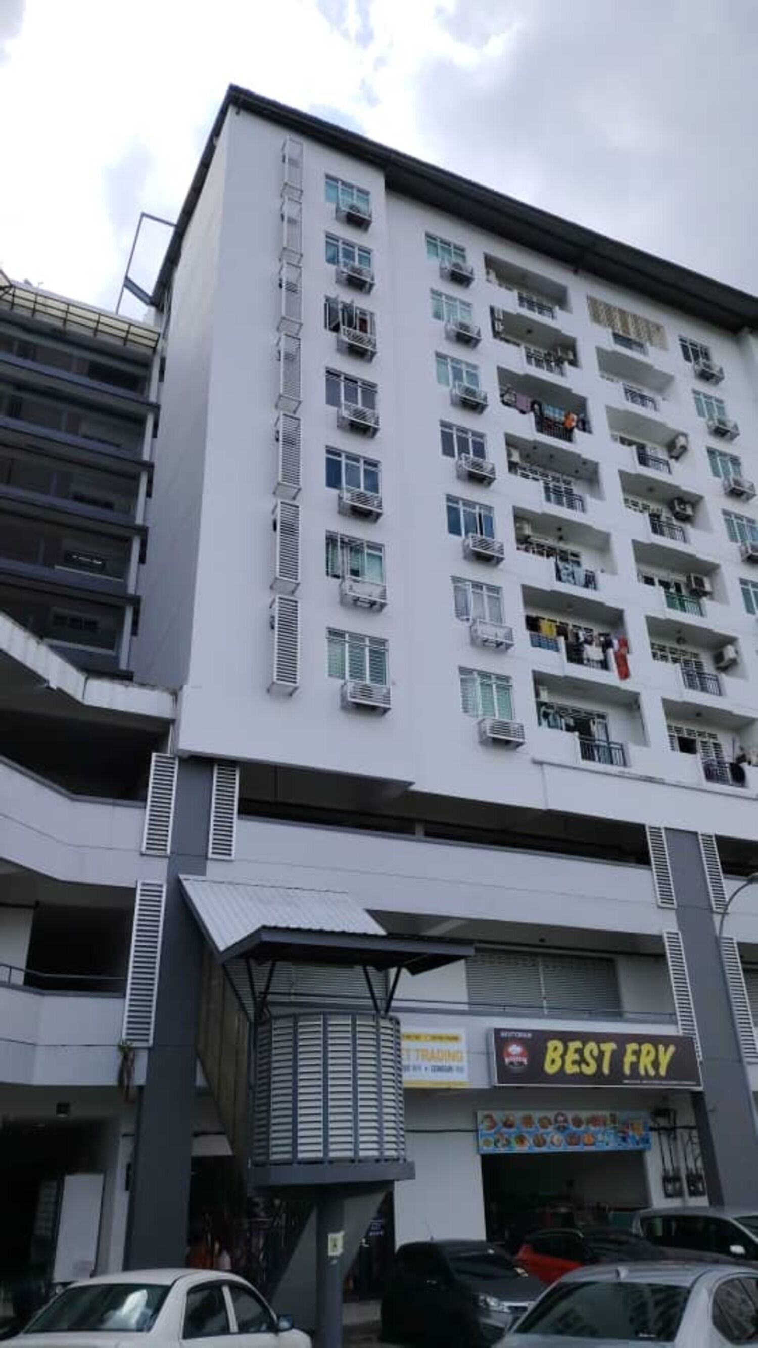 A multi-story building with balconies, a sign for 'Best Fry', and a covered area with a sign for 'Trading'.