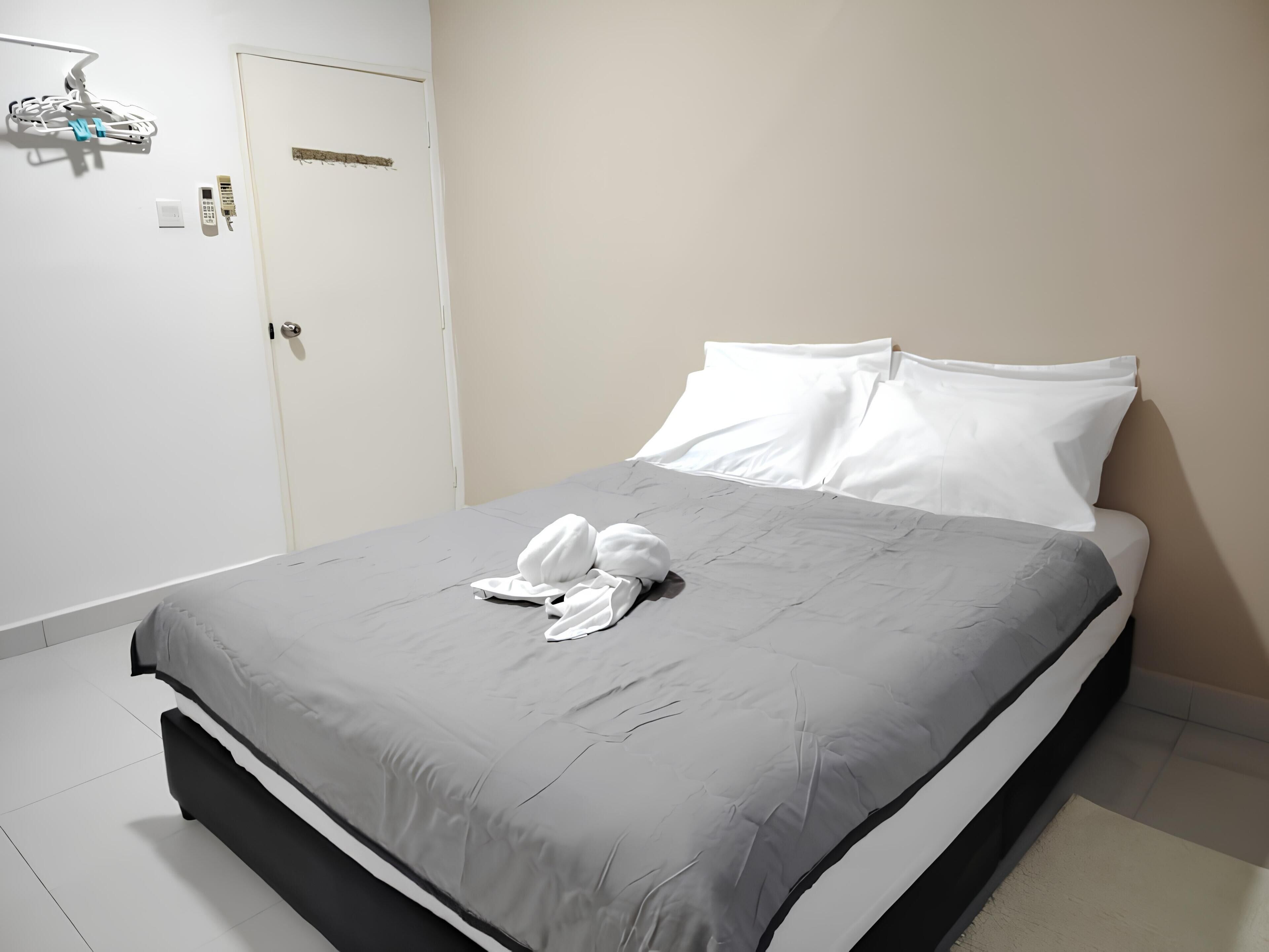 En snyggt bäddad säng med vita kuddar och ett grått överkast i ett hotellrum.