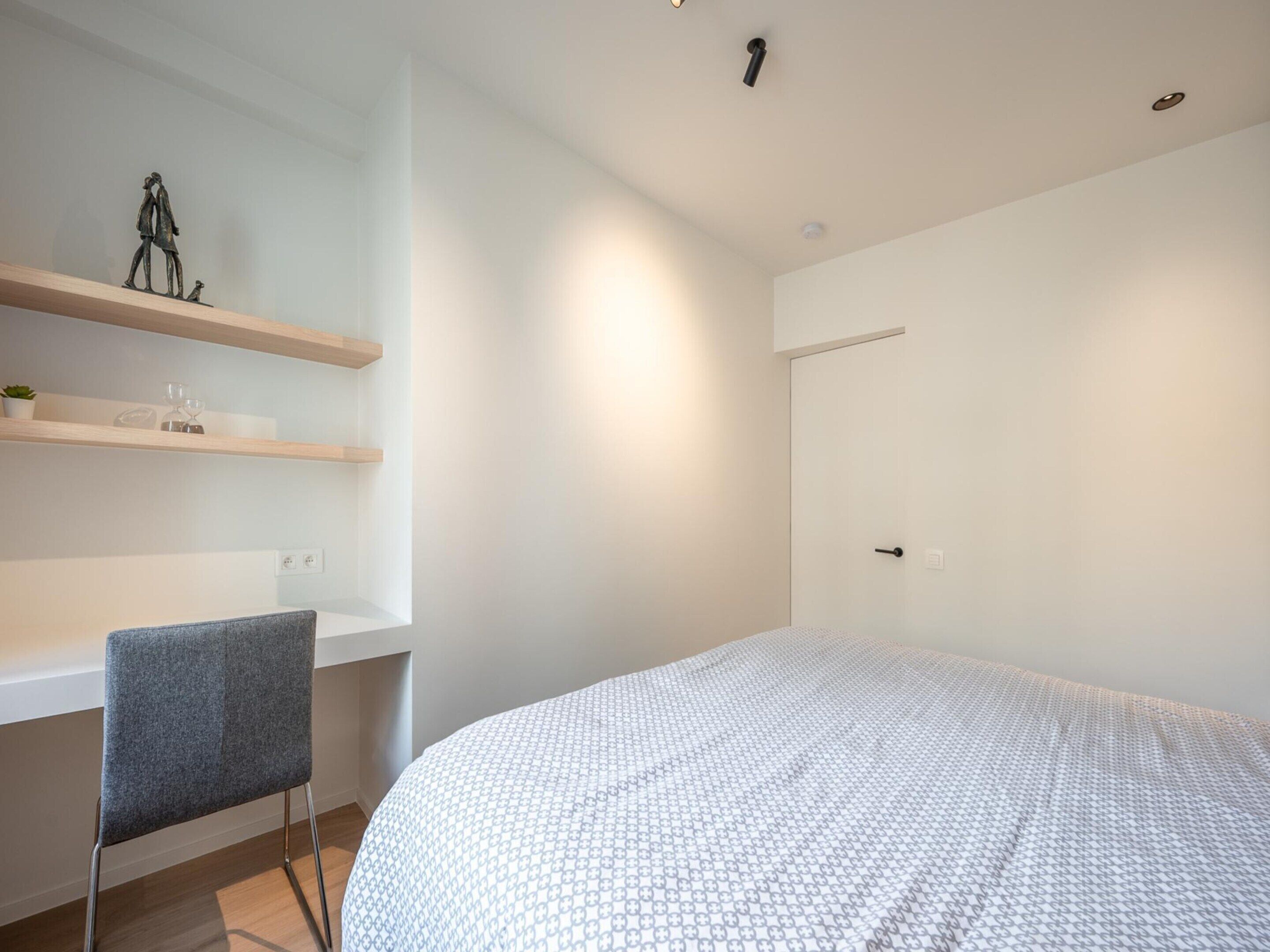 Ein Schlafzimmer mit einem Bett, einem Schreibtisch mit Stuhl sowie einem Regal mit Dekoration.