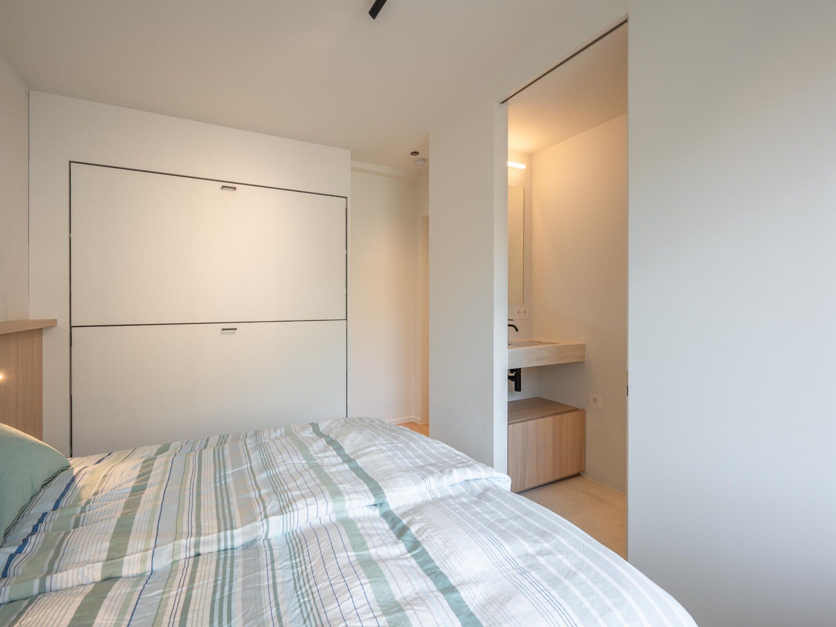 A bedroom with a bed, a built-in wardrobe, a mirror, and a small bathroom with a sink.