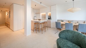 Et moderne køkken med en central ø, barstole og et spiseområde med bord og stole.