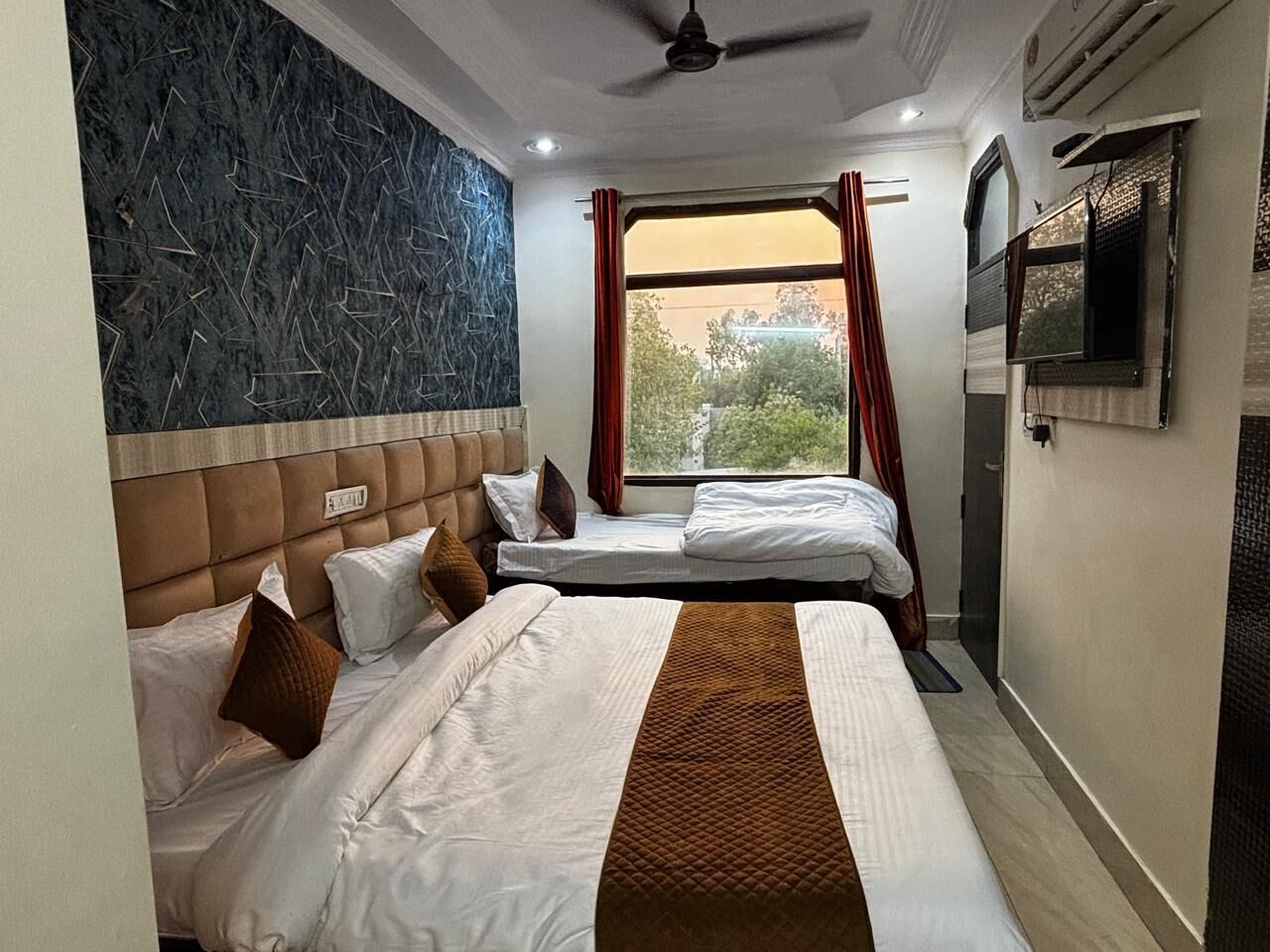 A hotel room with two beds, a ceiling fan, a TV, and a window with curtains.