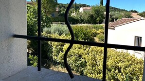 A balcony with a view of a garden, a white building, and trees.