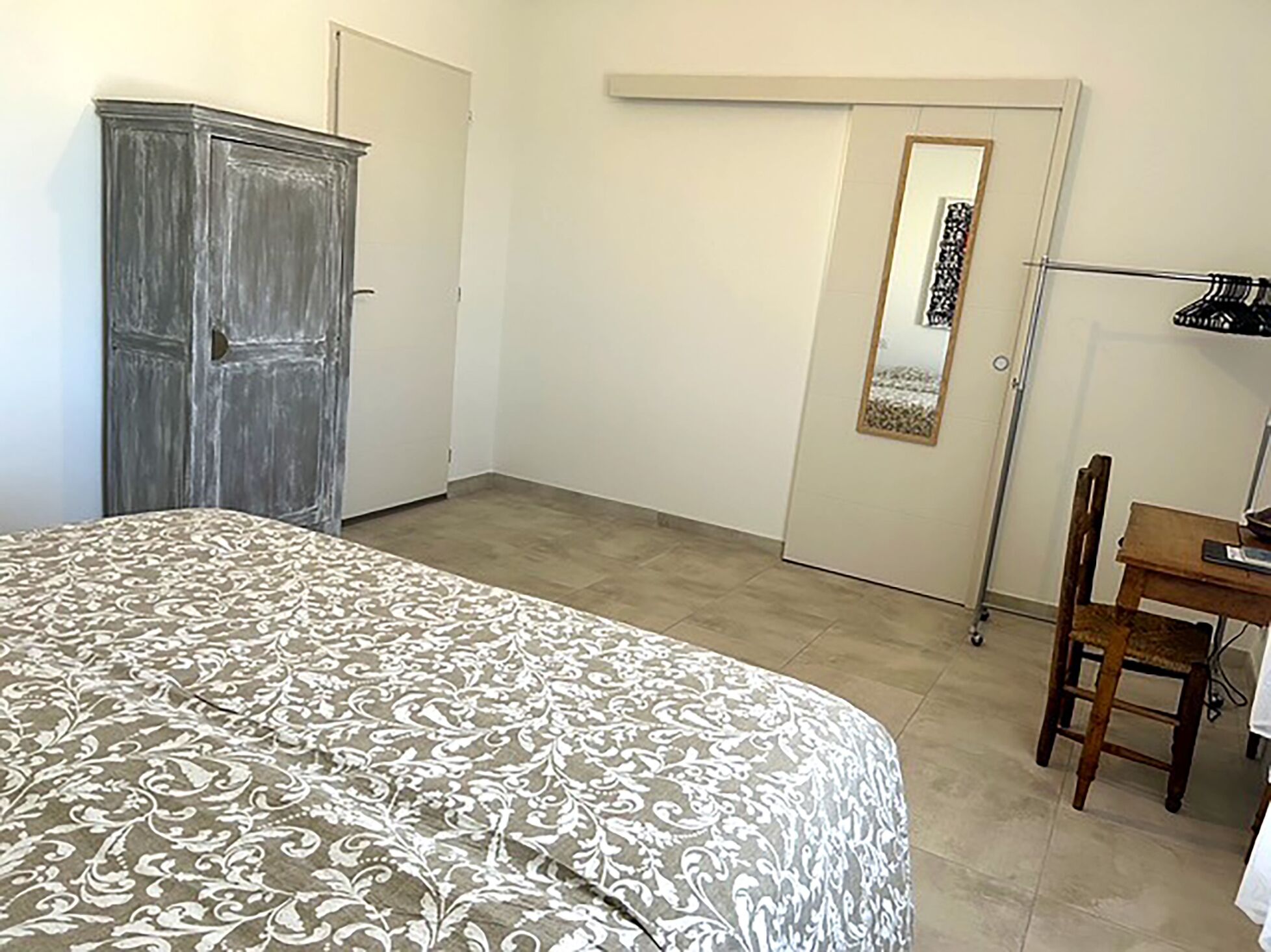 A bedroom with a bed, a wardrobe, a desk with a chair, and a door with a mirror.
