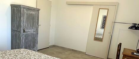 A bedroom with a bed, a wardrobe, a desk with a chair, and a door with a mirror.