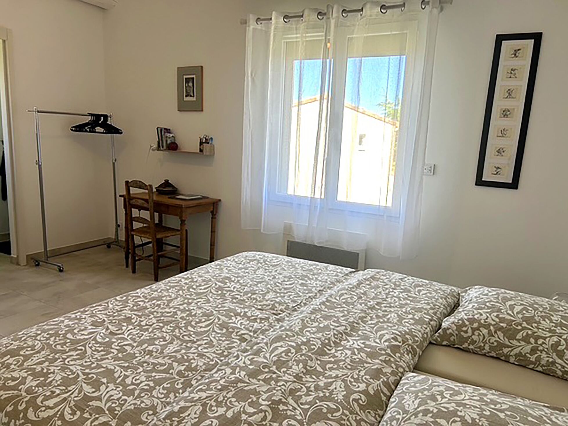 A bedroom with a bed, a desk, a chair, and a window with curtains.