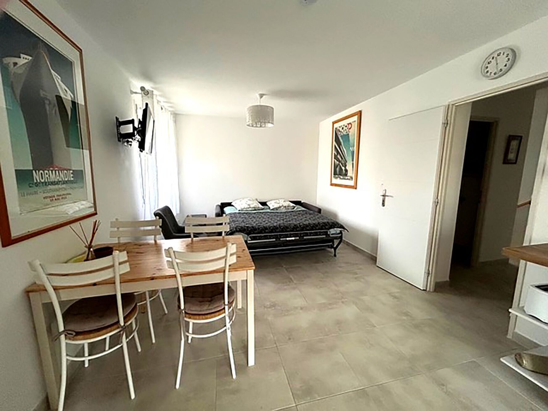 Une pièce comprenant un lit, une table à manger avec des chaises, une horloge au mur et un tableau encadré.