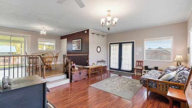 A spacious living room with hardwood flooring, a wooden sofa, a dining area with chairs, a staircase, and a large window with blinds. - Country Charmer (Sevierville)