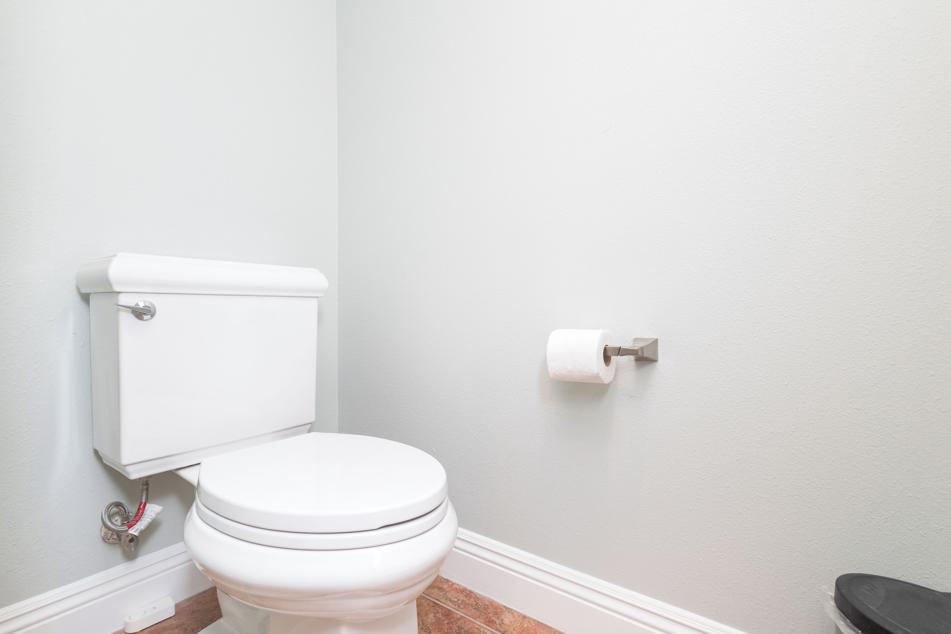 A white toilet with a tank, a roll of toilet paper on the wall, and a brown floor.