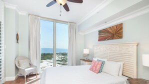 A bedroom with a large bed, a chair by the window, a nightstand, and a ceiling fan. - New Listing! Coastline Views P2-1603 (Pensacola Beach)