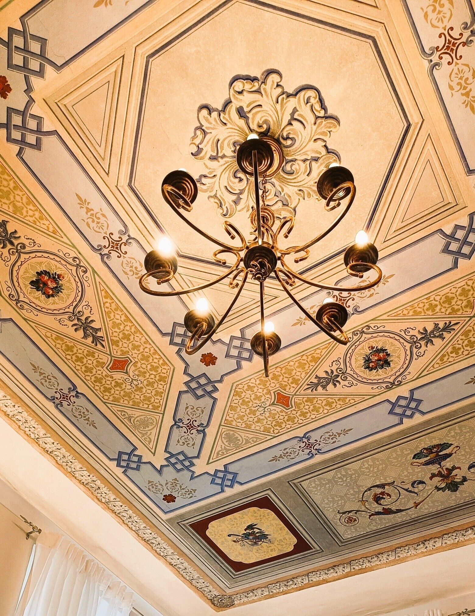 A ceiling with a chandelier and ornate patterns.