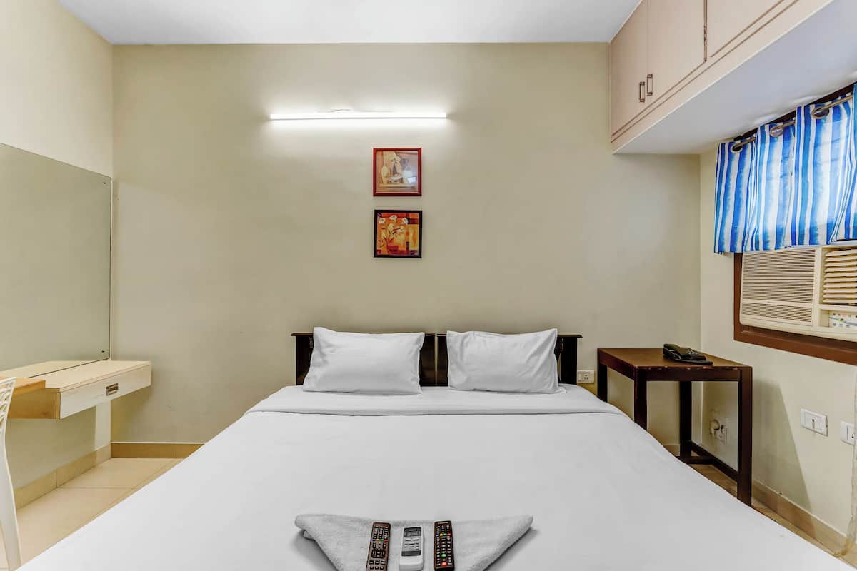 Een hotelkamer met een bed, een bureau, twee ingelijste foto's aan de muur, een nachtkastje met telefoon, en een raam met gordijnen.