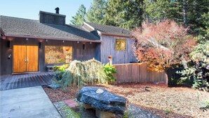 A wooden house with a large front door, a chimney, and a garden with a rock bench. - Seabreeze Sanctuary Sea Ranch Oasis! (Sea Ranch)