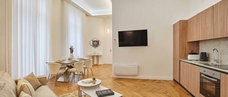 Un salon moderne comprenant un canapé, une table basse et un coin repas avec des chaises et une table. Il y a également une cuisine équipée de placards et d’une cuisinière.
