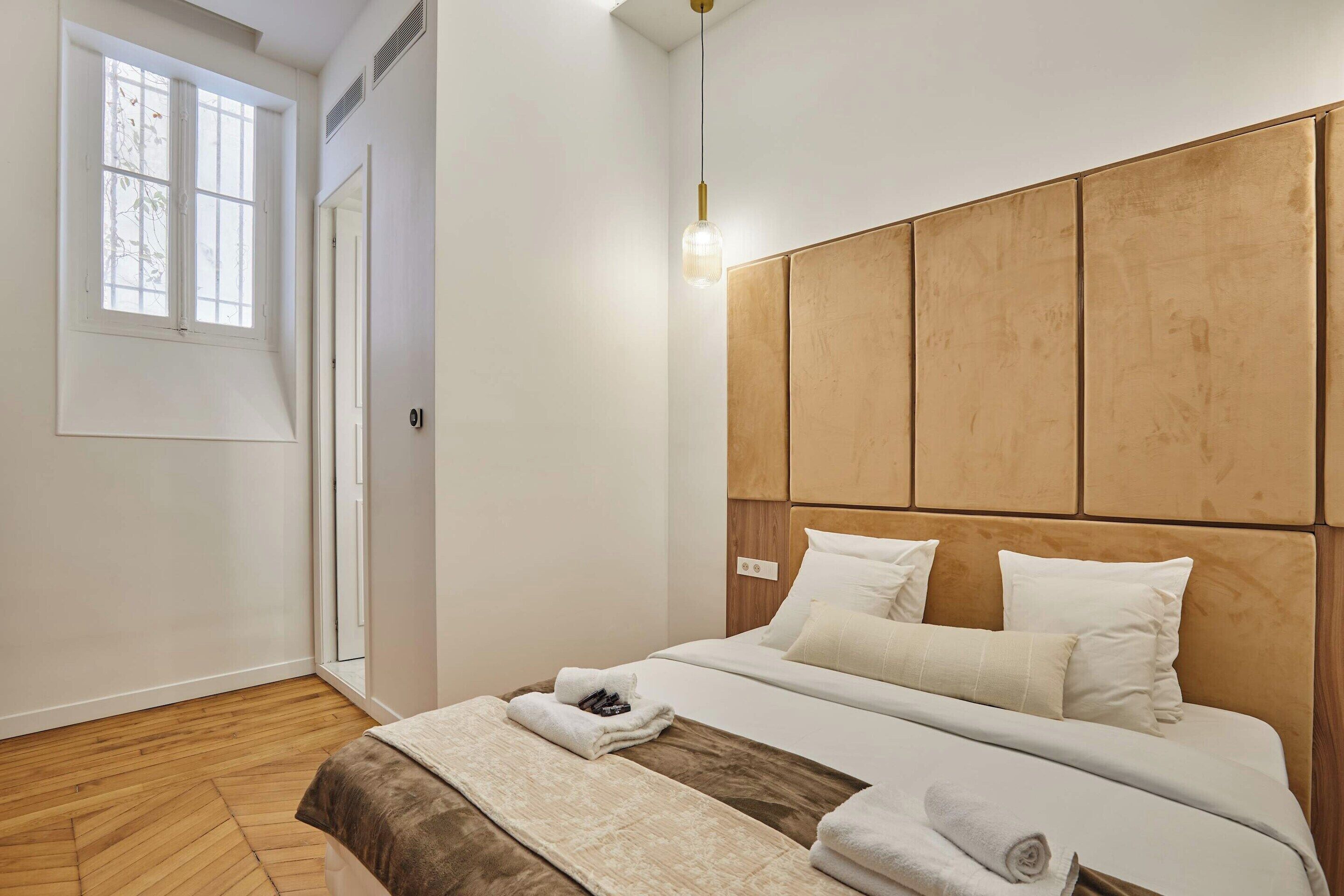 A bedroom with a wooden headboard, a large window, and a bed with white bedding.