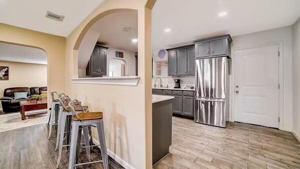 A modern kitchen with stainless steel appliances, a dining area with bar stools, and a living room with a sofa and coffee table. - dog-friendly home with fenced yard, grill, sunroom (San Antonio)