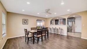 A spacious dining area with a wooden table and chairs, a ceiling fan, and a view into the kitchen area. - dog-friendly home with fenced yard, grill, sunroom (San Antonio)