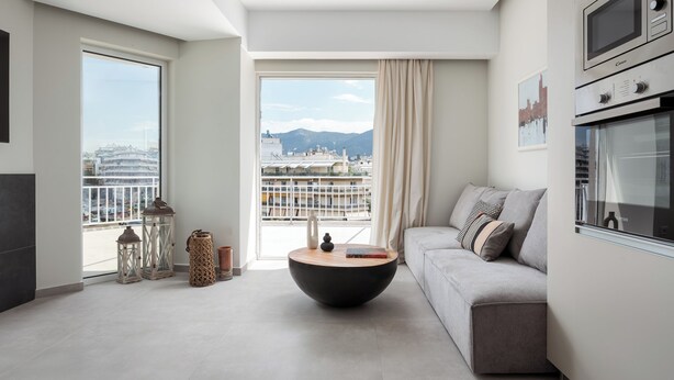 A modern living room with a round coffee table, a grey sofa, and a large window offering a city view. - Athens Luxury Ethereal View (Zografos)