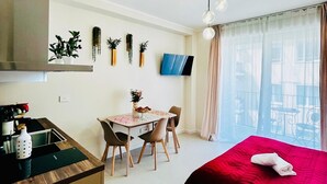 Una camera d'albergo con un letto, una scrivania con sedie, una TV e un balcone con tende.