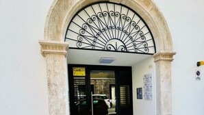 Ingresso di un edificio con arco in pietra e decorazione a sole in metallo sopra la porta.