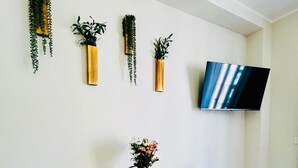 Zona pranzo con tavolo apparecchiato per due, sedie, un vaso con fiori e un televisore a schermo piatto montato a parete.